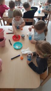 Dzieci wykonują kosmos w butelce wykorzystując kolorową wodę, watę, brokaty i cekiny gwiazdkowe.