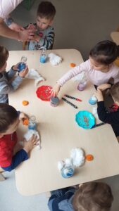 Dzieci wykonują kosmos w butelce wykorzystując kolorową wodę, watę, brokaty i cekiny gwiazdkowe.